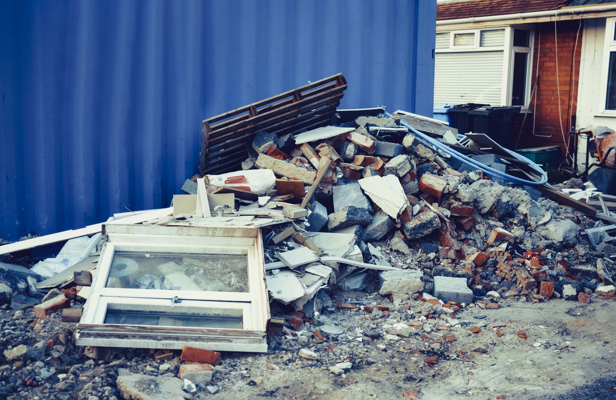A pile of construction waste near private house. Building rubble, bricks, stones. Junk, garbage piled up near the building. Street scene. Recycling industry, rubbish removal and collection service